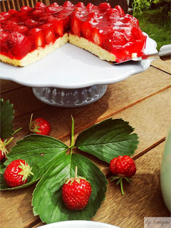 Erdbeertorte auf Tortenständer mit Erdbeerblättern und Erdbeeren